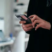 Close-up of a person using a smartphone indoors, with a blurred background of a desk and computer.