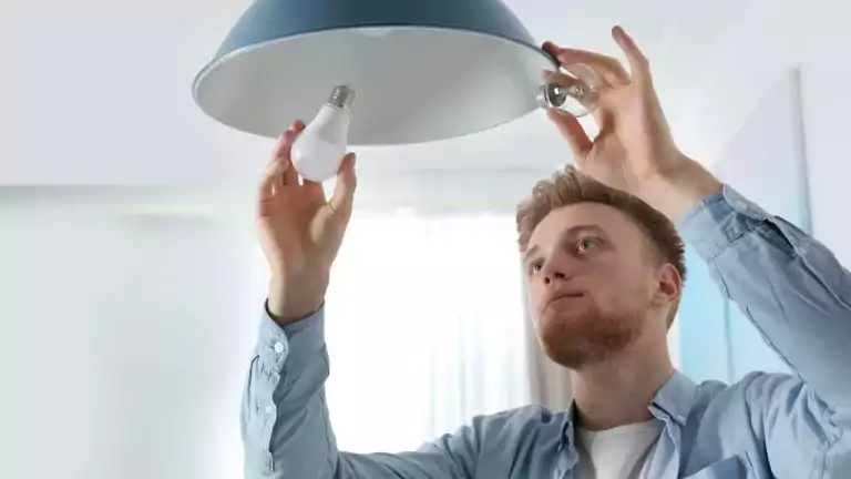 Man changing standard light bulb to an LED light bulb in an indoor pendant lamp.