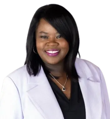 Smiling woman with straight black hair wearing a white blazer over a black top, accessorized with a silver necklace and hoop earrings, standing against a plain background.